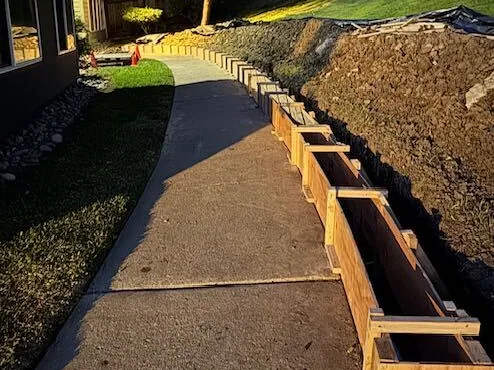 Timber forms set in a trench for a long concrete curb wall beside a sidewalk