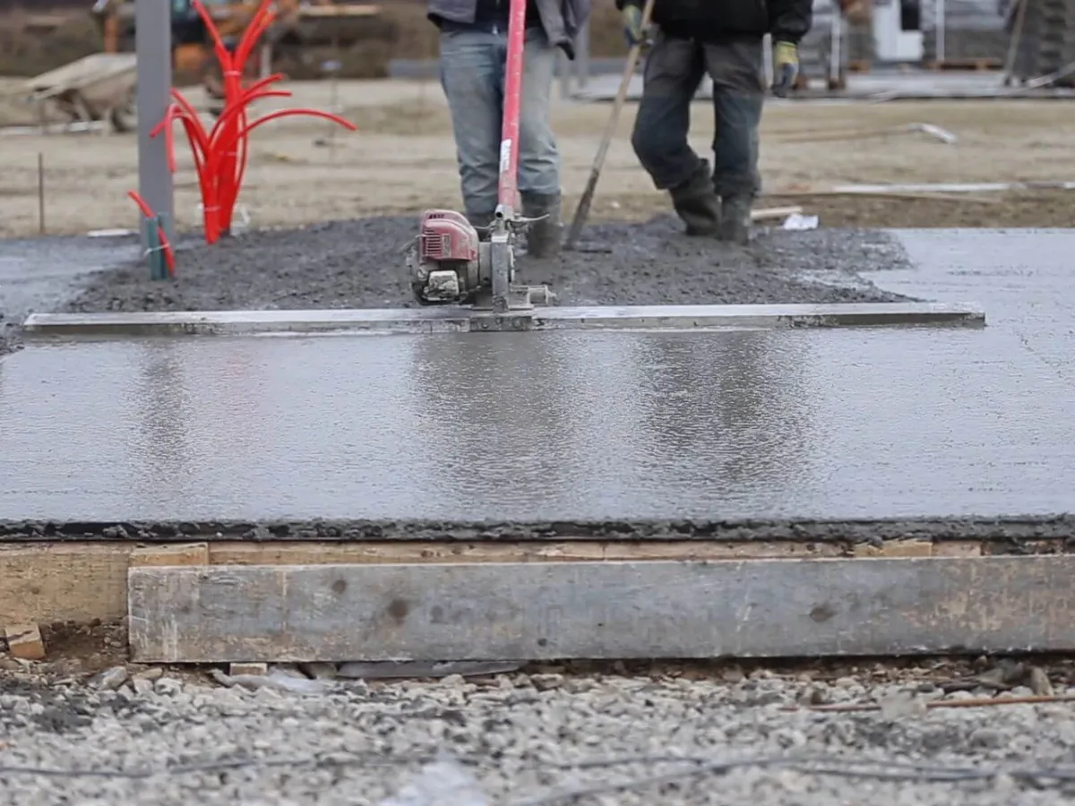 Workers pulling a vibrating screed across freshly poured concrete