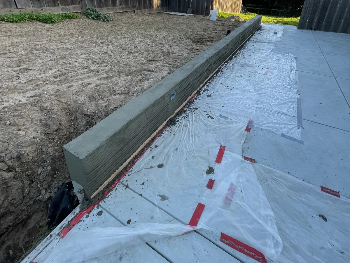Long concrete wall beside a fresh slab curing under plastic sheeting