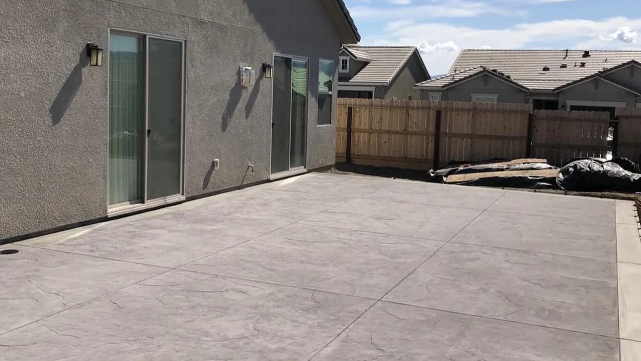 Finished textured concrete patio running the full width of a fenced backyard