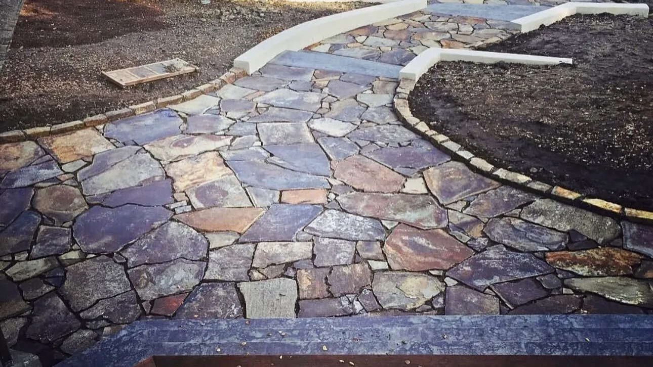 Flagstone patio finished with a curved stone border beside a wood deck