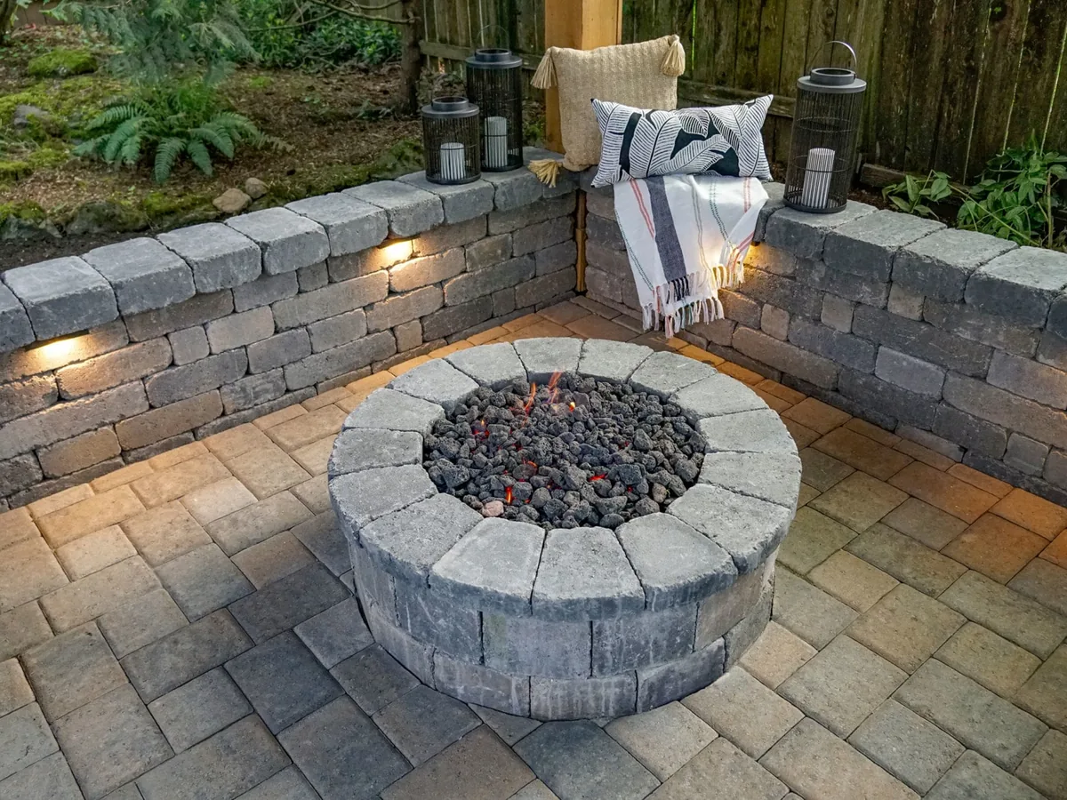 Gas fire pit with cut stone cap and lava rock on pavers