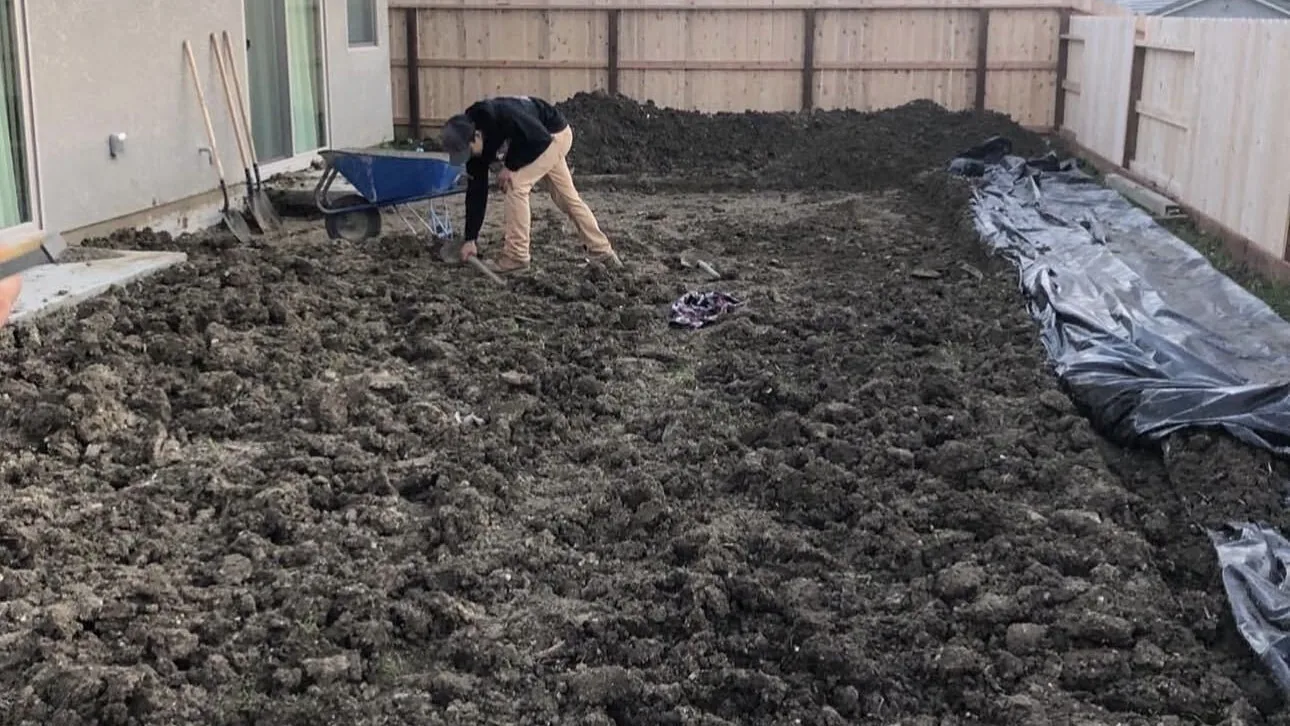 Worker breaking up a backyard with a mattock before the base goes in