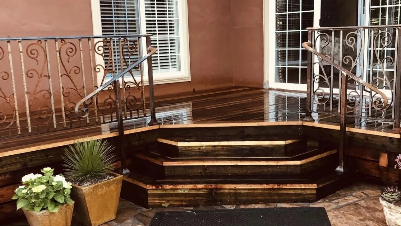 Redwood deck steps with scrolled iron railings opening onto a flagstone patio