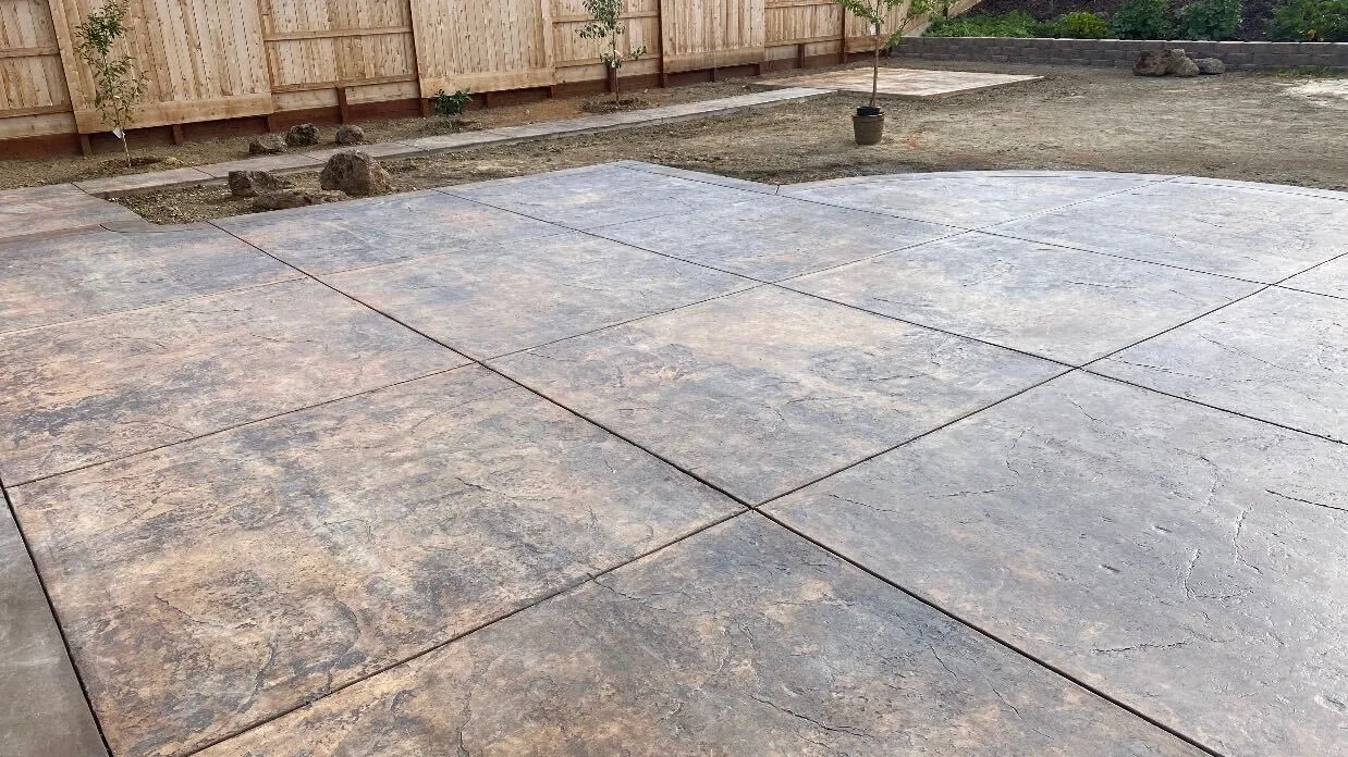 Wide colored stamped concrete patio finished up to a new fence line