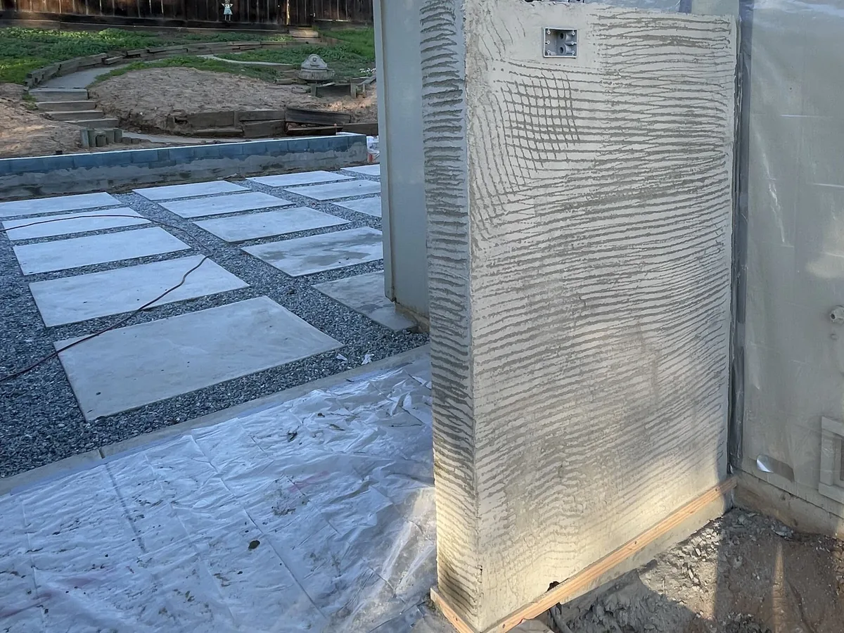 Lath and scratch coat going on a site wall next to large-format concrete pads