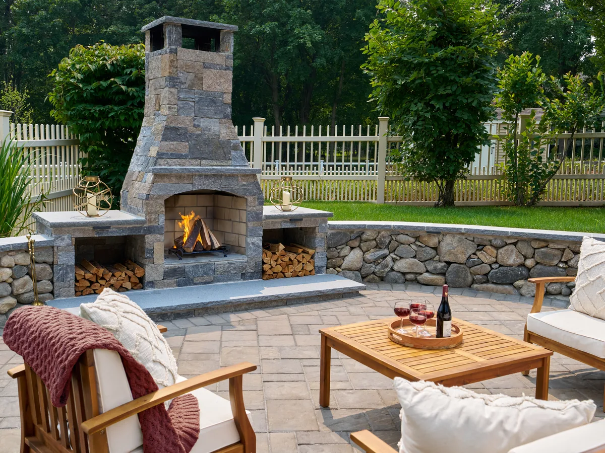 Stone outdoor fireplace with chimney and hearth beside a lawn and patio