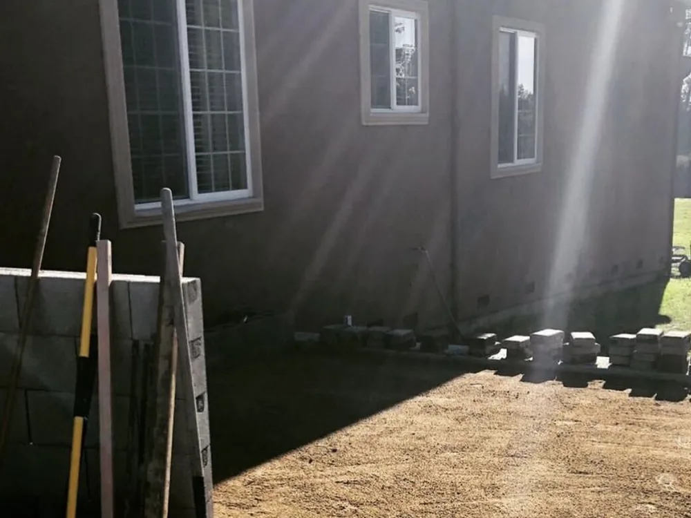 Compacted gravel base prepared next to a block wall and stucco house