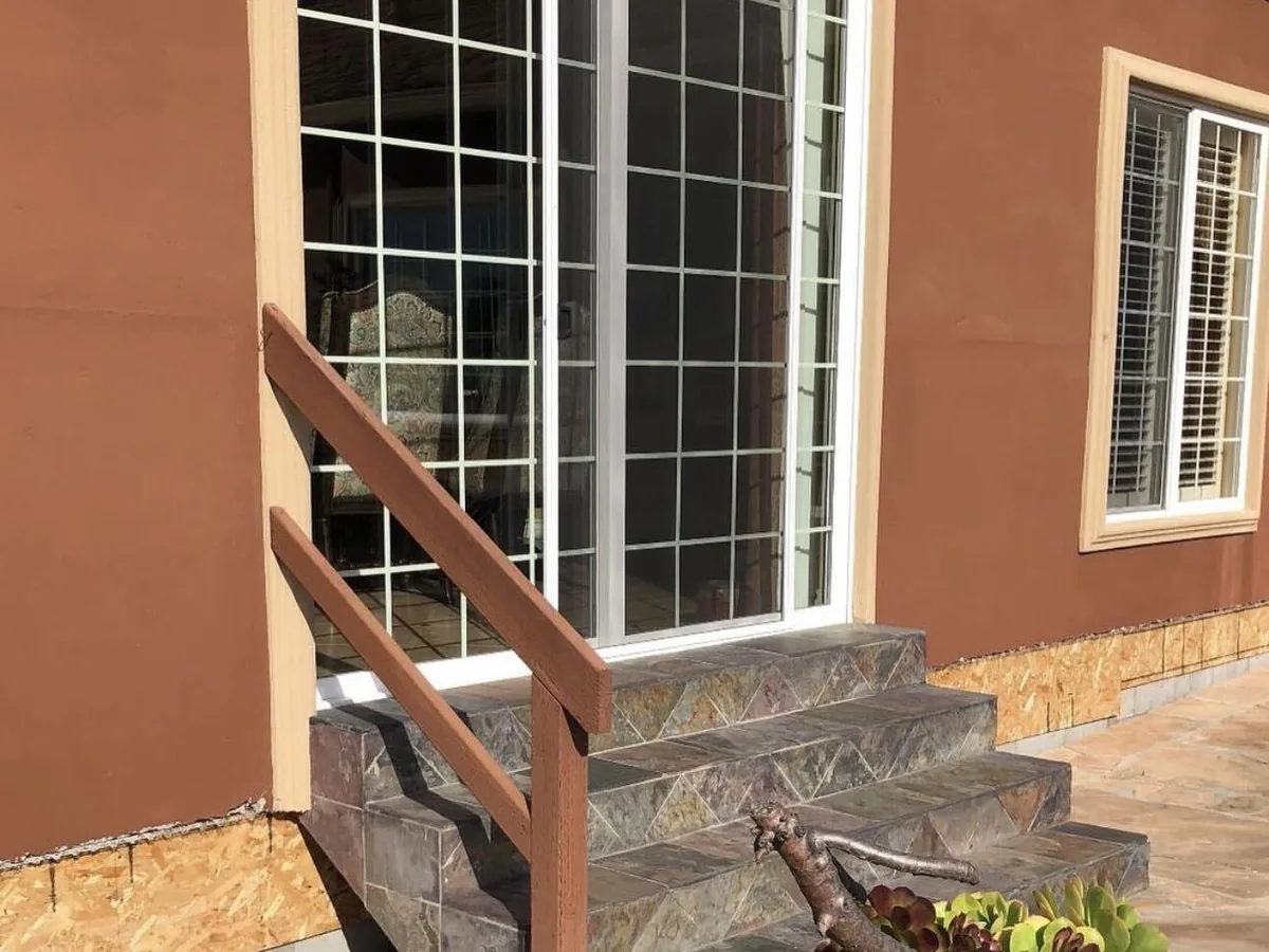 Slate tile entry steps with a stained wood handrail against a stucco wall