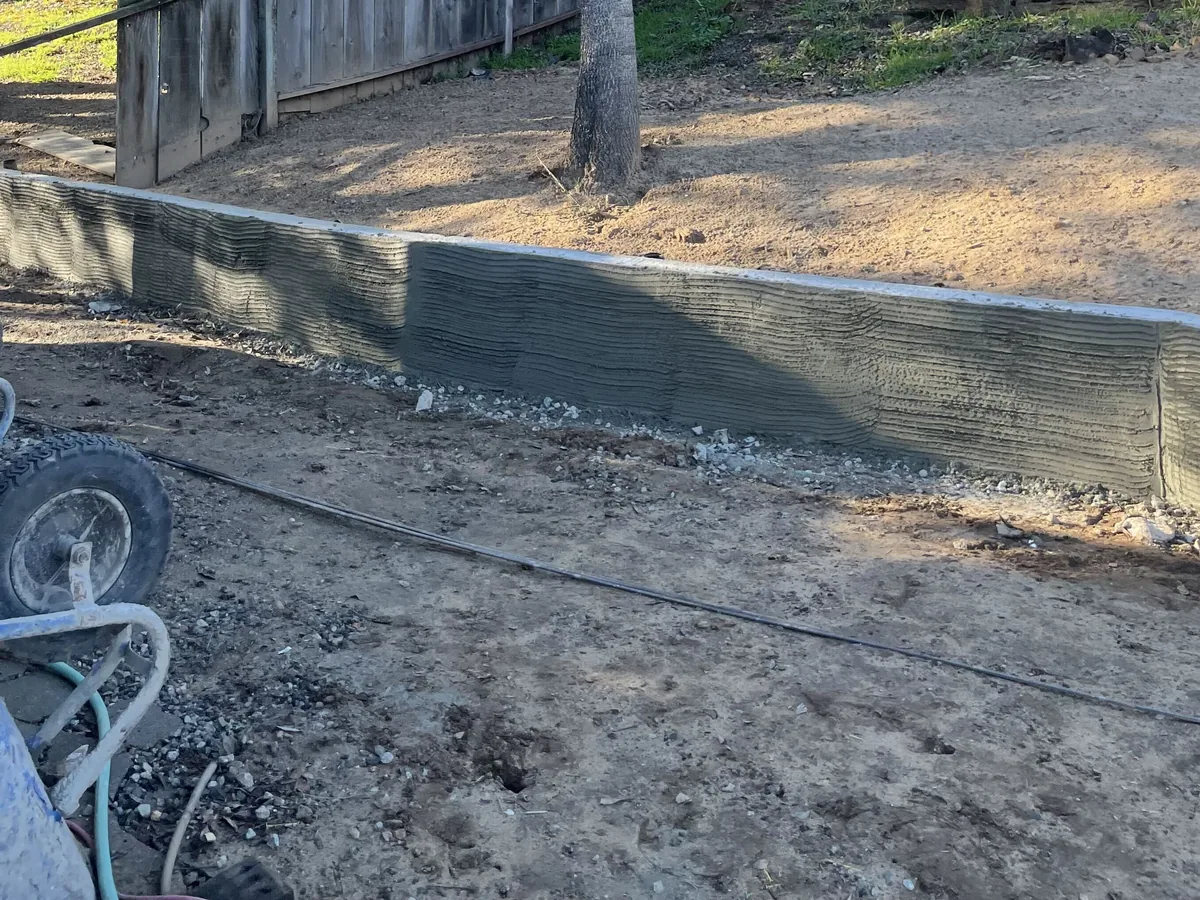 Low poured retaining wall running along a fence line around a mature tree